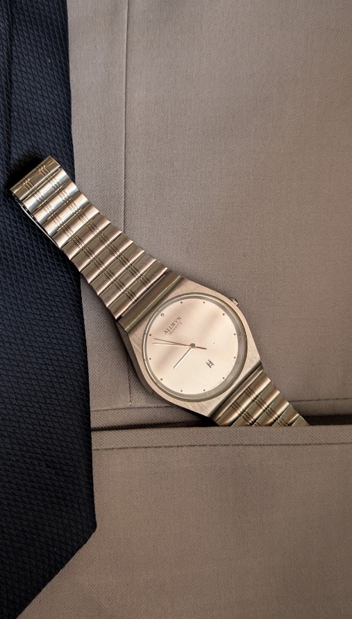 allwyn quartz silved brushed dial vintage watch with minimalistic integrated look. The image shows watch placed over a sand gray suit and navy blue tie, giving it a beautiful look with formals